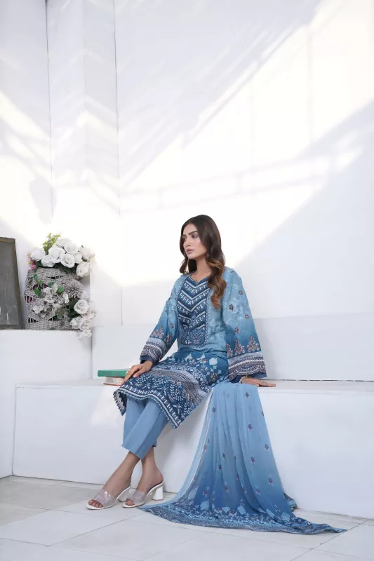 Woman in a powder blue embroidered suit with a long dupatta, seated on a white step in a bright room