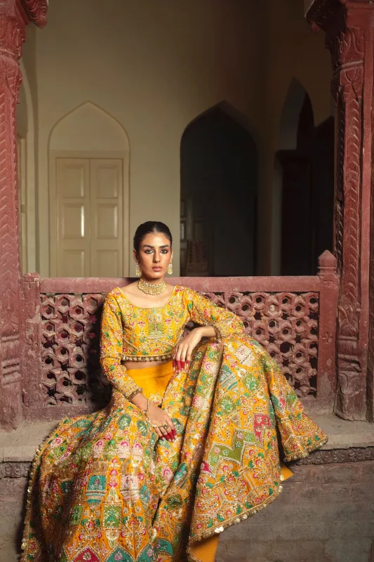 Woman in a mustard yellow multicolour printed lehenga standing in a haveli courtyard