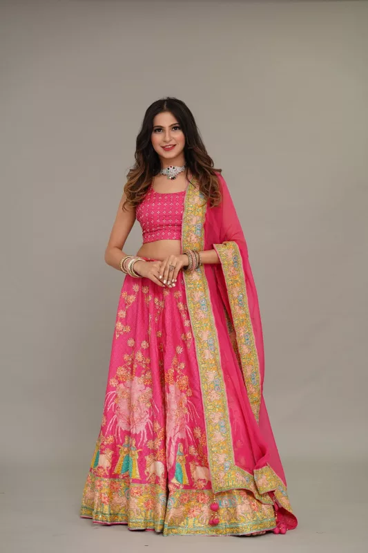 Woman in a fuchsia pink floral lehenga with a gold-bordered dupatta, in a studio