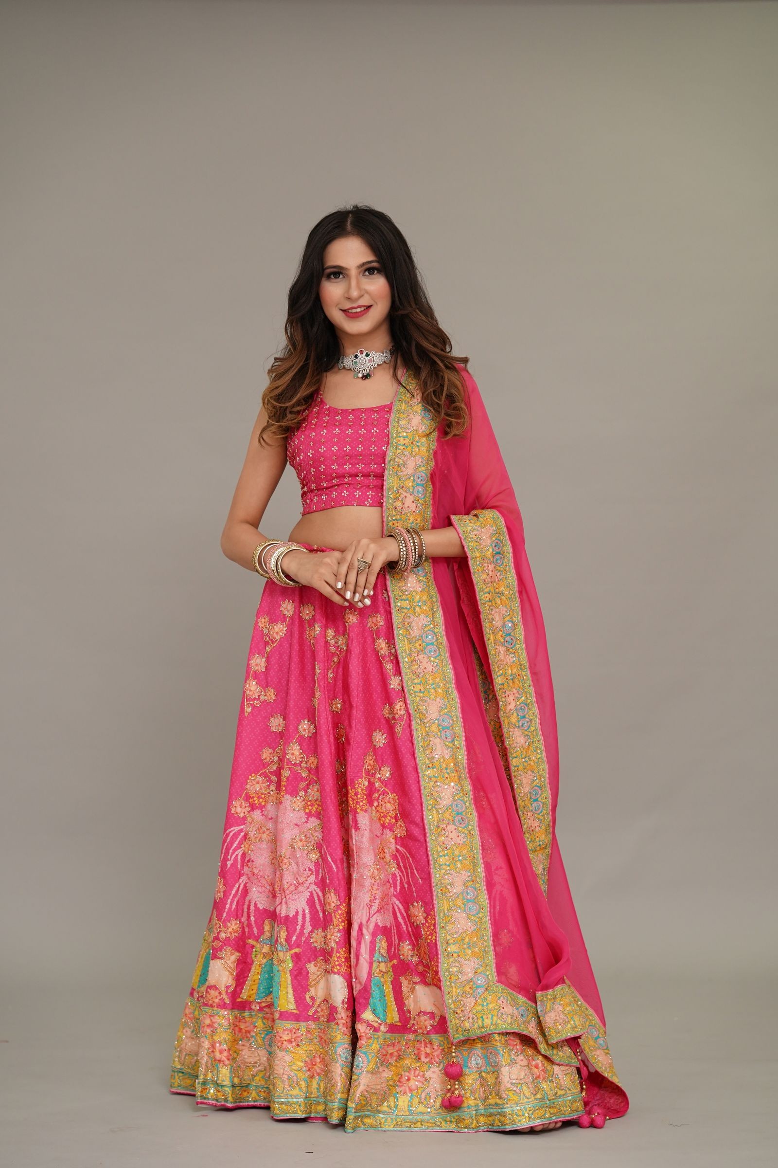 Woman in a fuchsia pink floral lehenga with a gold-bordered dupatta, in a studio