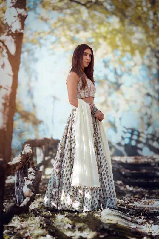 Woman in an ivory printed lehenga with a sleeveless blouse, standing in a green forest setting