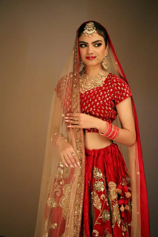 Bride in a red lehenga with a gold blouse and gold net dupatta, wearing bridal jewellery