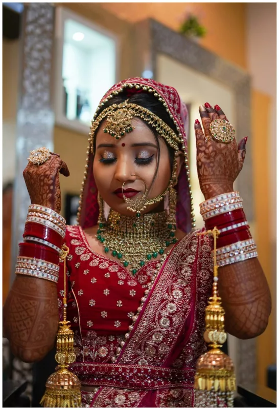 Close portrait of a bride in a crimson bridal lehenga blouse with gold embroidery and a veil dupatta, holding kaleere