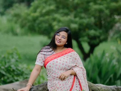 Woman in a white saree with a red border and floral print, standing in a garden