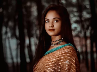 Woman in a copper brown silk blend saree with a teal border, standing among trees