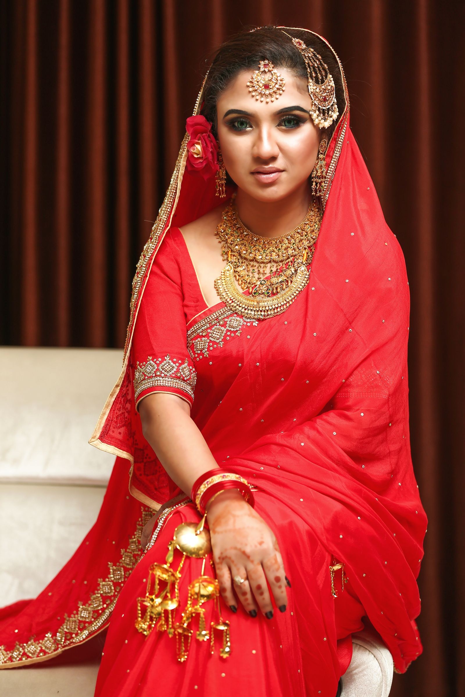 Woman seated in a red bridal saree with a gold embroidered border, wearing bridal jewellery