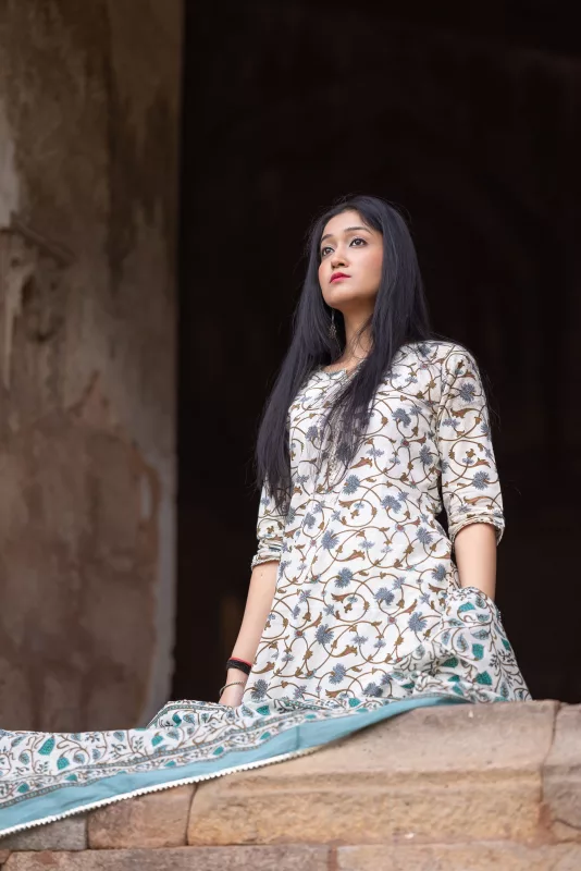 Woman seated in an ivory printed Anarkali kurta set with a teal border dupatta