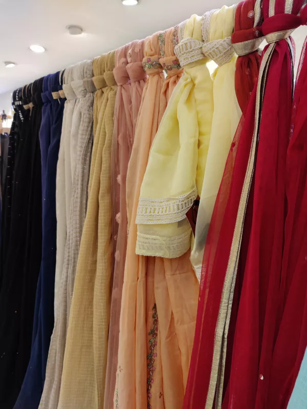 A rack of pastel and red dupattas on hangers