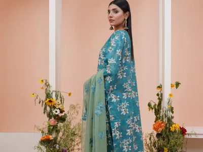 Woman in a teal floral printed straight suit with a sage green dupatta, standing between flowers under pink arches