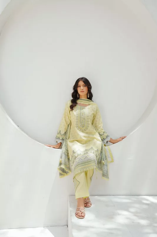 Woman in a pastel lemon embroidered straight suit with a matching dupatta, seated in a white studio arch