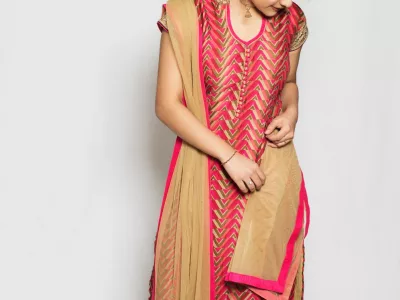 Girl in a pink and gold churidar-style suit with a gold net dupatta, standing in a white studio